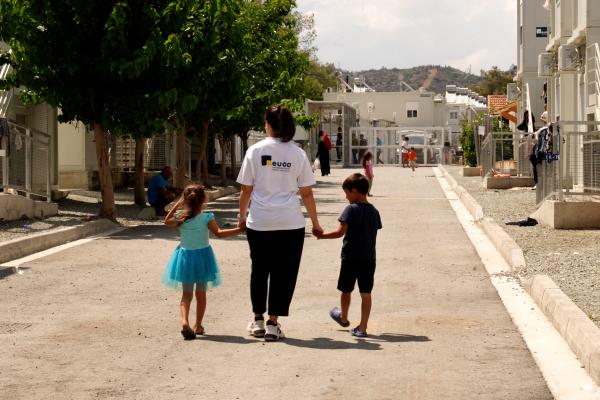 EUAA staff member accompanying two young children in the Kofinou Reception Centre in Cy[rus.